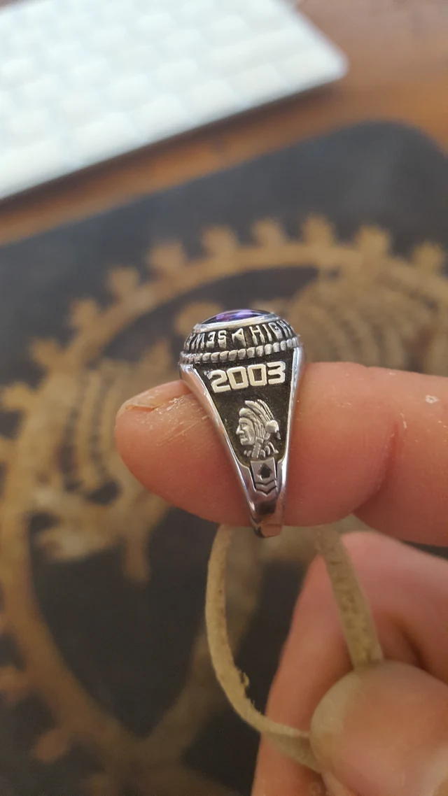 A hand holding a silver ring in front of a dark and gold circular design.