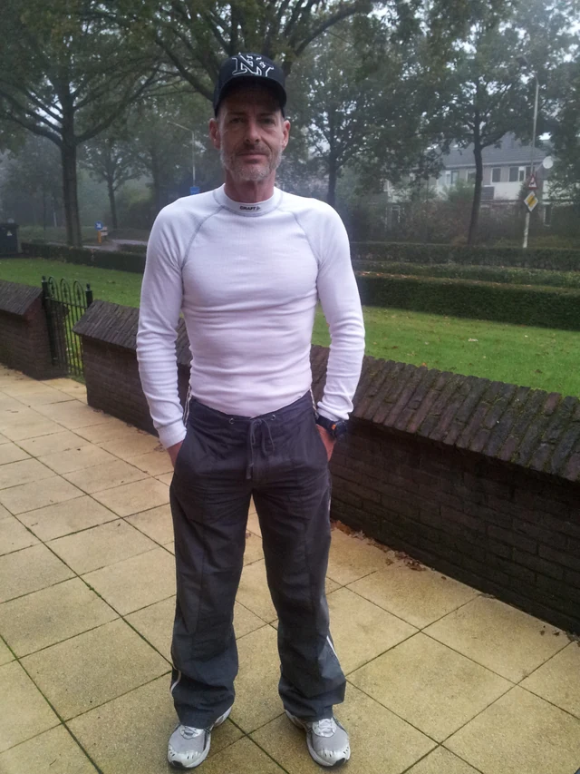 A person in a pale sweater standing on a paved path beside a garden.