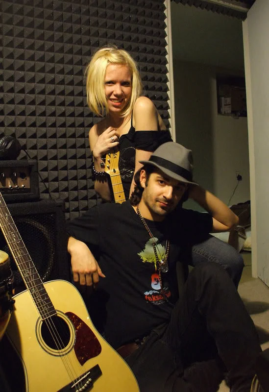 A person in a grey hat seated in front of another person holding a guitar.